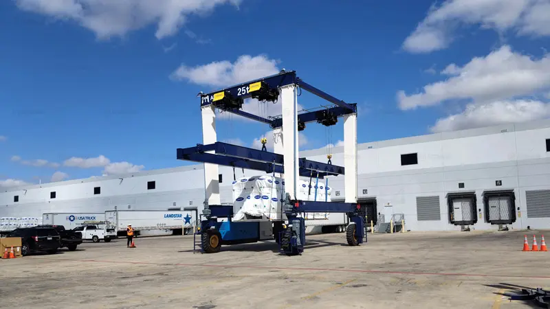 Grúa pórtico sobre neumáticos Aicrane DTLS25T manipulando unidades industriales de climatización en EE. UU.